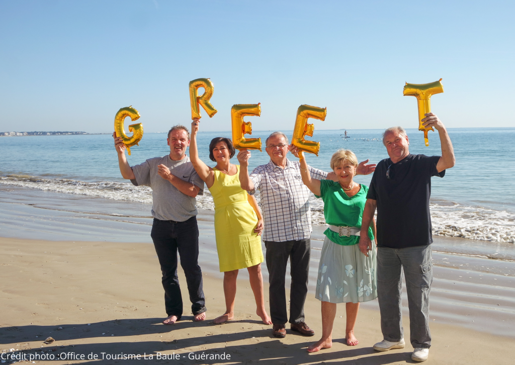 Cinq Greeters posent avec les lettres du mot "Greet" sur une plage de Guérande