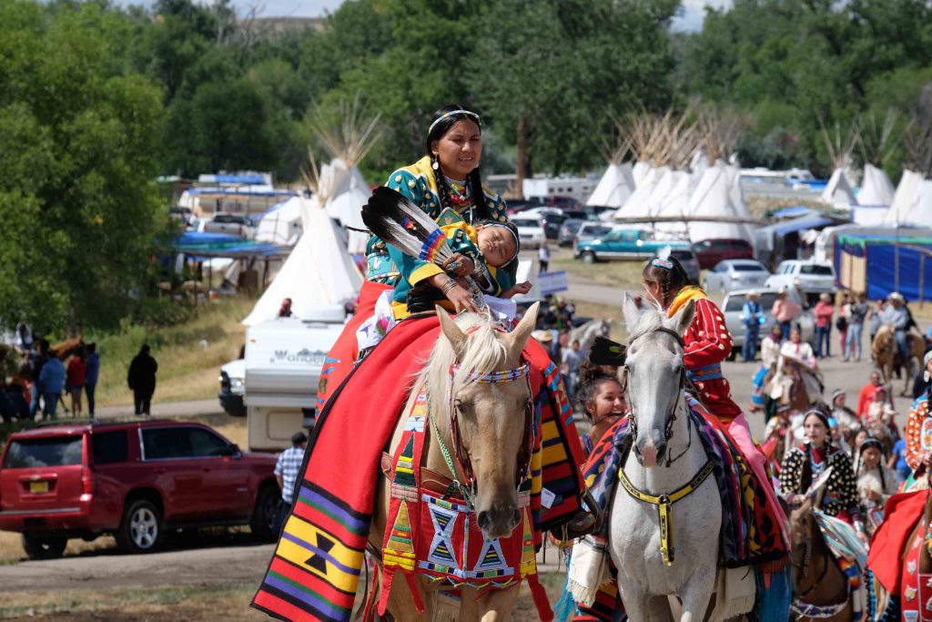 Une femme est habillé en tenu traditionnel des indiens d'amérique, elle est à cheval avec son enfant.