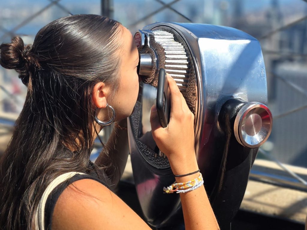Femme observant New York depuis l’Empire State Building avec jumelles panoramiques